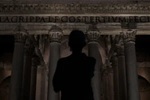 Man stands before ancient roman pantheon at night.