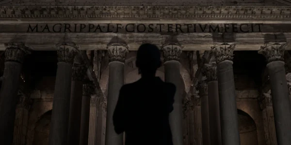 Man stands before ancient roman pantheon at night.