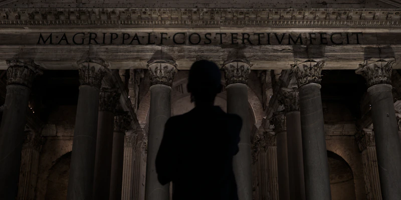 Man stands before ancient roman pantheon at night.