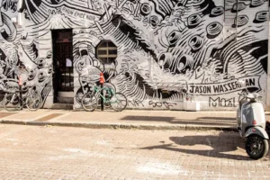 A vibrant black-and-white mural featuring bicycles and a scooter on an urban street.