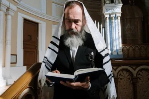 Elderly man in traditional shawl reading a book inside a synagogue