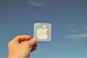 a hand holding an apple sticker in front of a blue sky