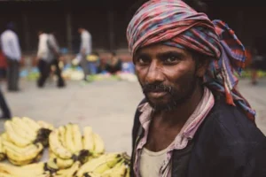 Portrait of a vendor selling bananas at an urban market, displaying cultural attire.