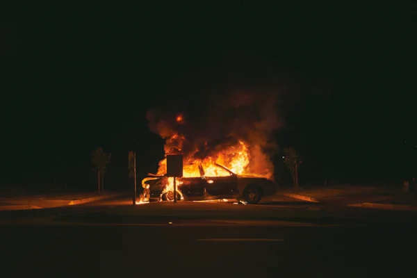burning grey sedan near trees and signboard at night