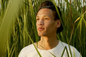 A young man stands peacefully among tall grass in a sunlit meadow, embodying relaxation.