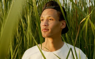 A young man stands peacefully among tall grass in a sunlit meadow, embodying relaxation.