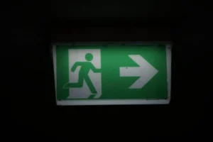 Illuminated green emergency exit sign with an arrow pointing right in a dark setting.