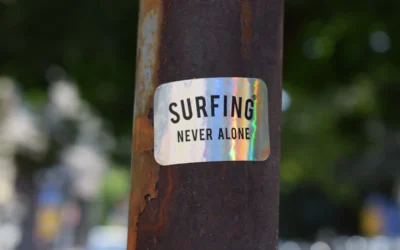 A surfing sticker is placed on a rusty pole.