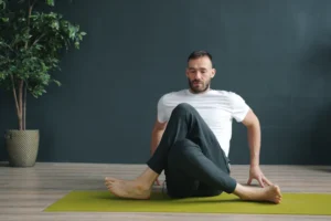 Man in white shirt twists body on yoga mat.