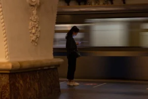 A woman standing on a subway platform texting as a train moves by, showcasing urban lifestyle.